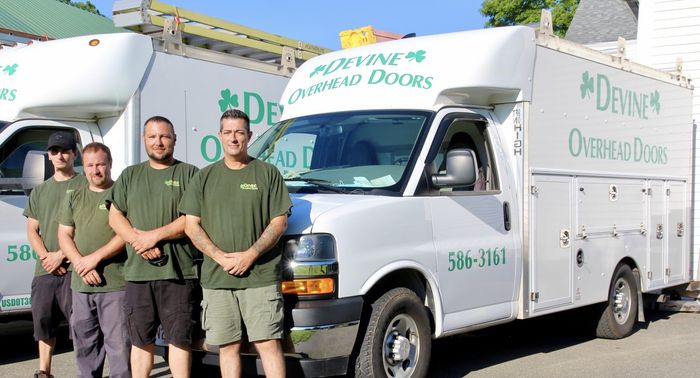 Four men in green shirts stand by two work trucks with company logo, 