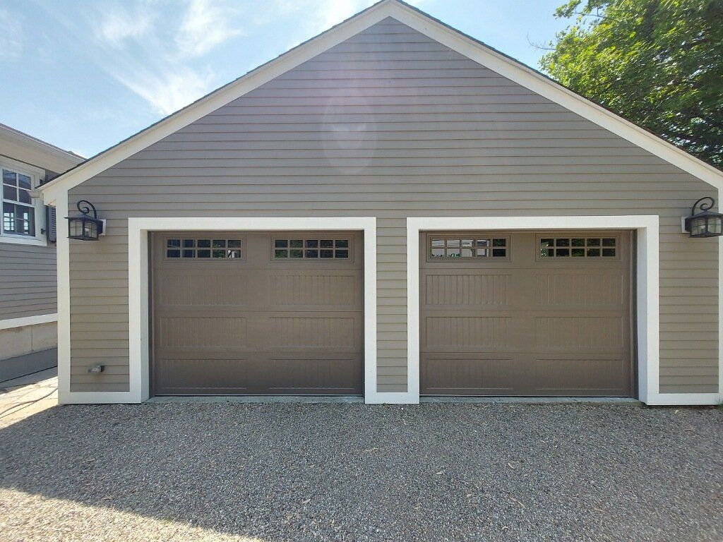 Two-car garage with brown doors, gray siding, and a gravel driveway.