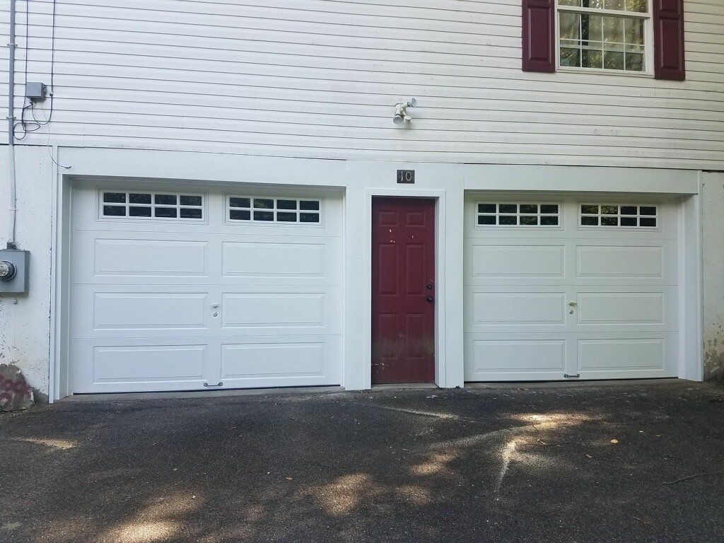 White garage with two doors and a maroon door in between. White siding and dark asphalt driveway.