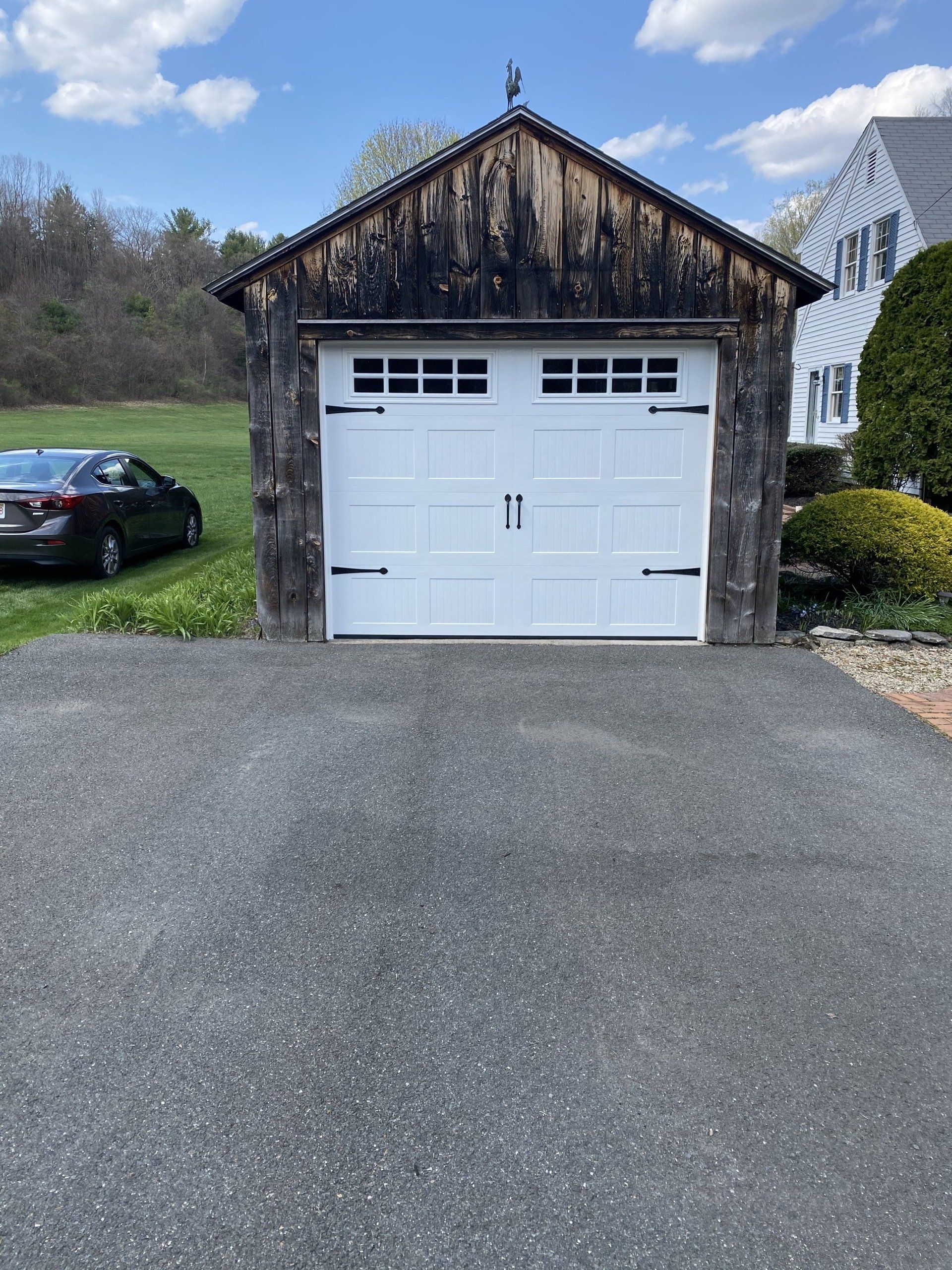 White garage door in a stone building on a paved driveway with a car parked nearby.