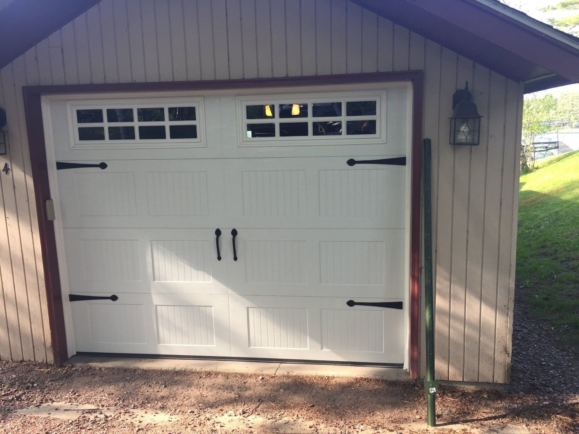 White garage door with decorative black hardware and windows, set in a light beige building.