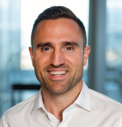 Man with short dark hair and a white shirt smiles, office backdrop.