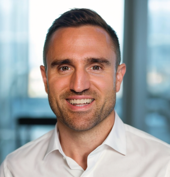 Man with short dark hair and a white shirt smiles, office backdrop.