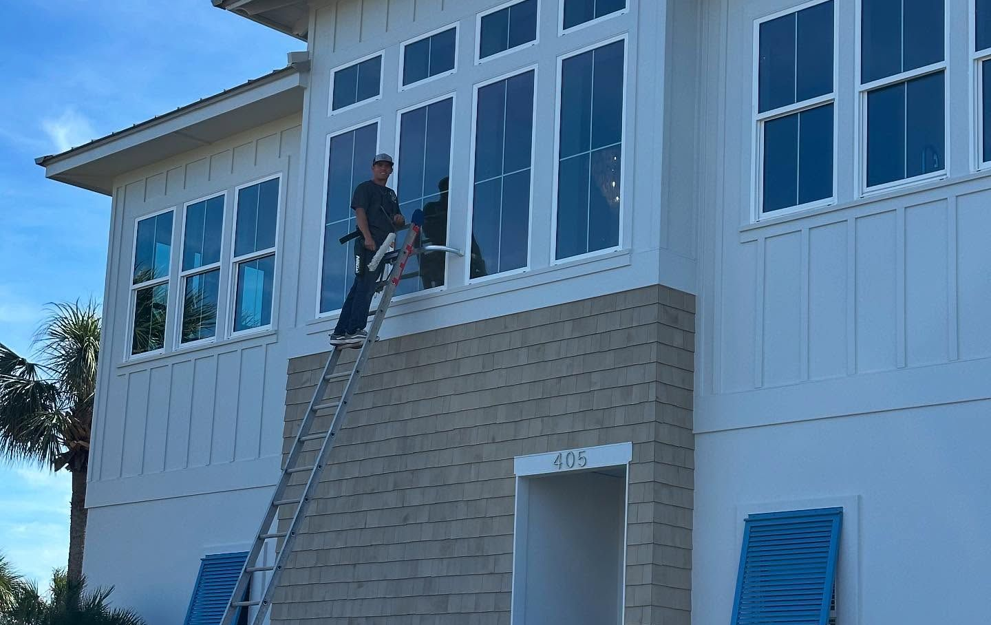 Person on a ladder washing windows of a two-story house with white siding.