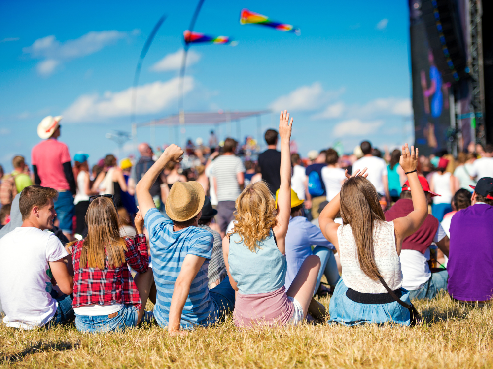 A crowd of people are sitting in the grass at a music festival.