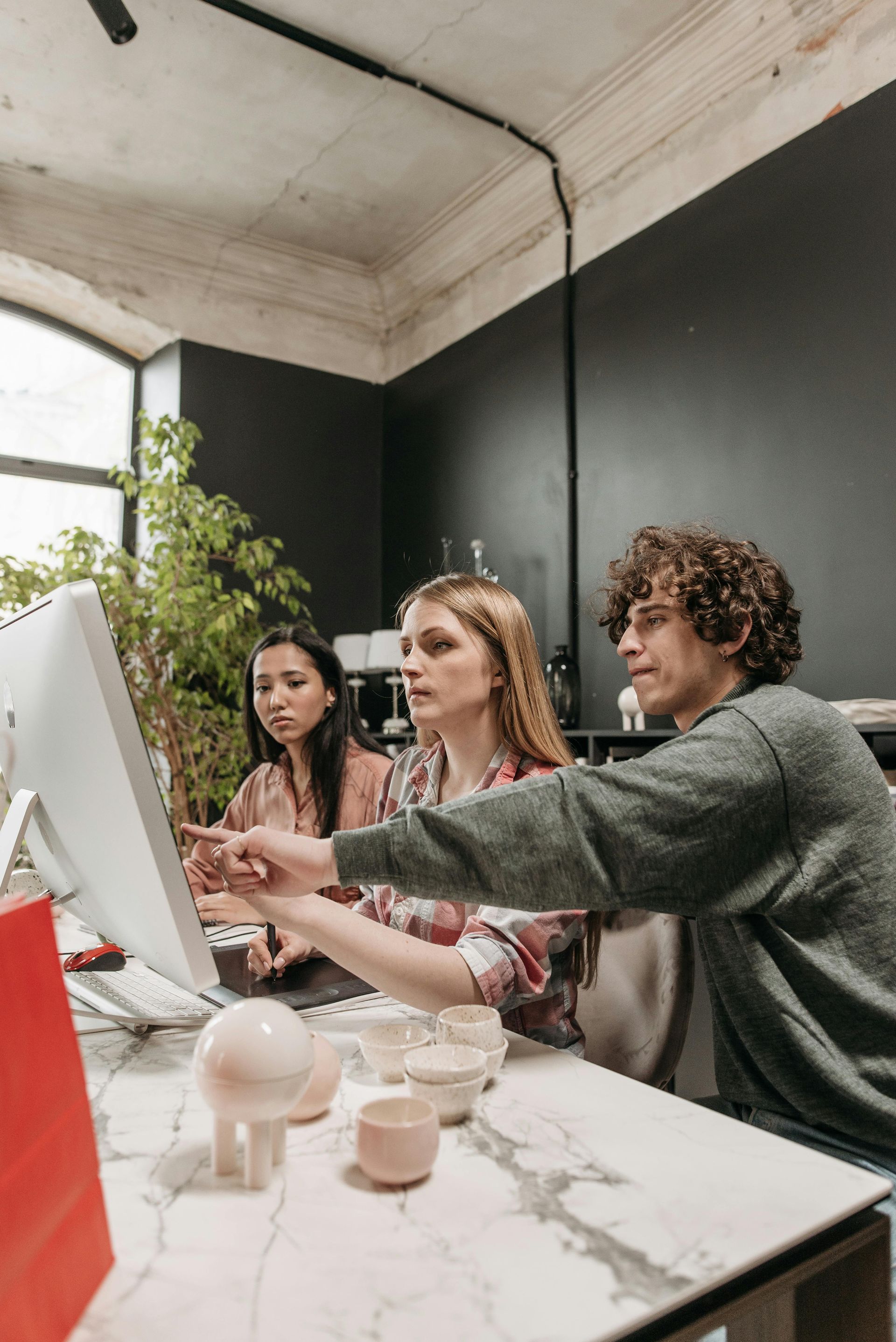 Three coworkers collaborating at a white desk in a modern office, looking at a large desktop monitor