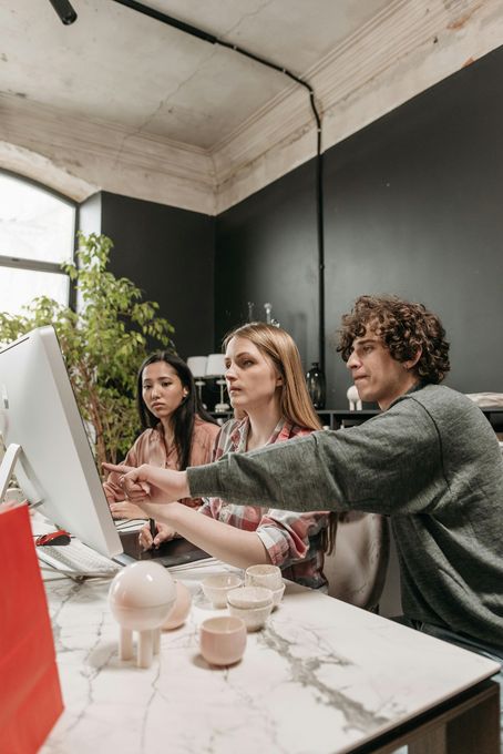 Three coworkers collaborating at a white desk in a modern office, looking at a large desktop monitor