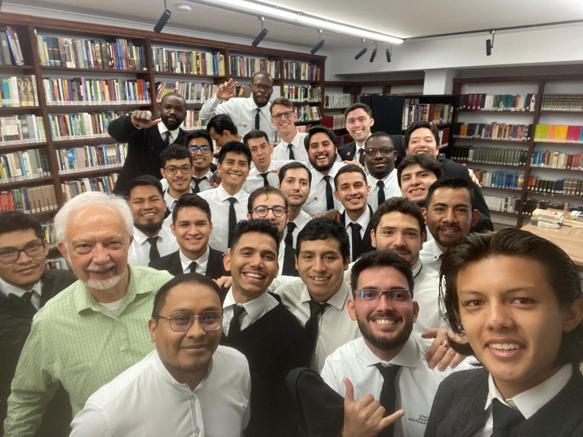 Group of men in suits pose in a library, smiling and looking at the camera.