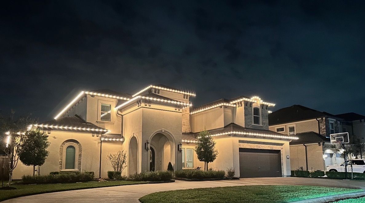 Luxury stucco house at night, warmly lit with string lights and a manicured front lawn
