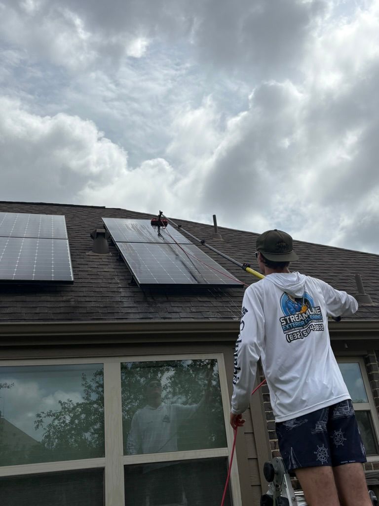 Person on a ladder inspecting solar panels on a house roof under cloudy sky