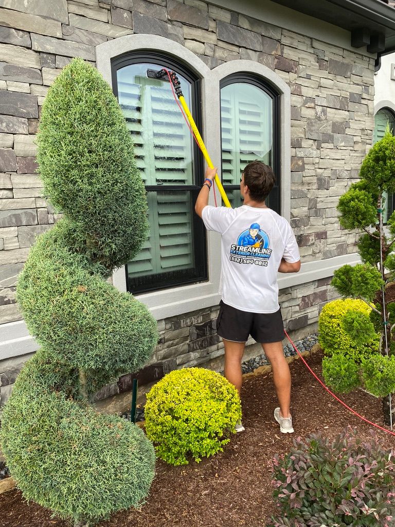 Person using a long yellow pole to clean a window on a stone house exterior.