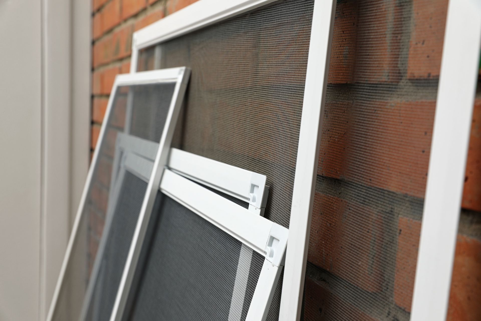 Window screens leaning against a brick wall outdoors