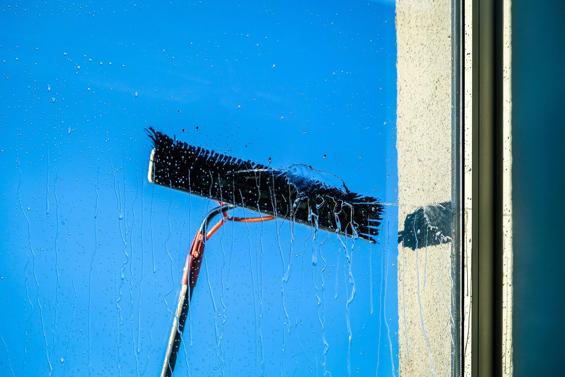 Window squeegee cleaning a blue glass pane beside a cream-colored frame