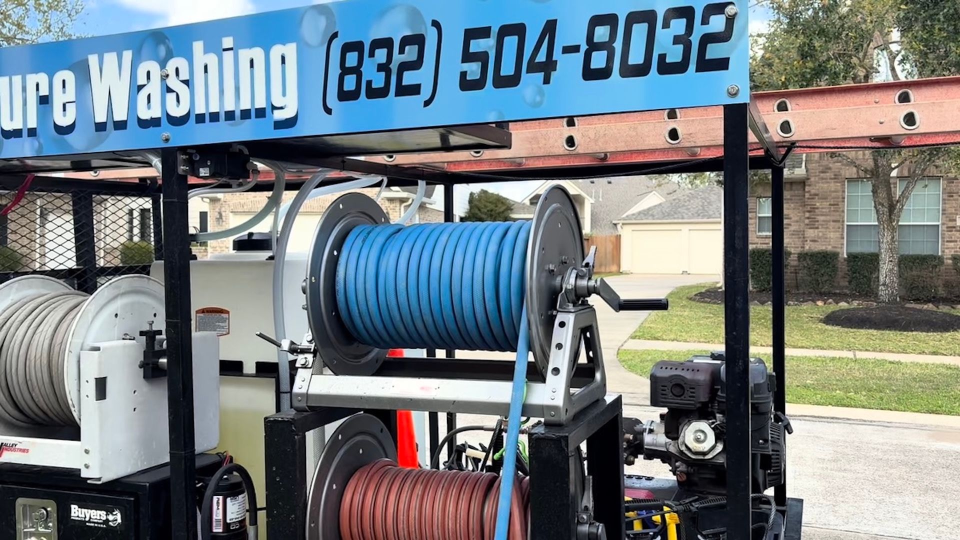 Pressure washing trailer with blue and red hose reels and a company sign above