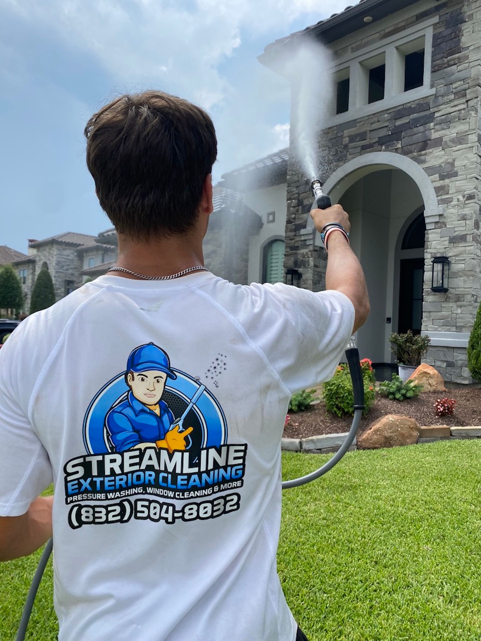 Person pressure washing a stone house exterior on a sunny day with a large streamline logo on their shirt