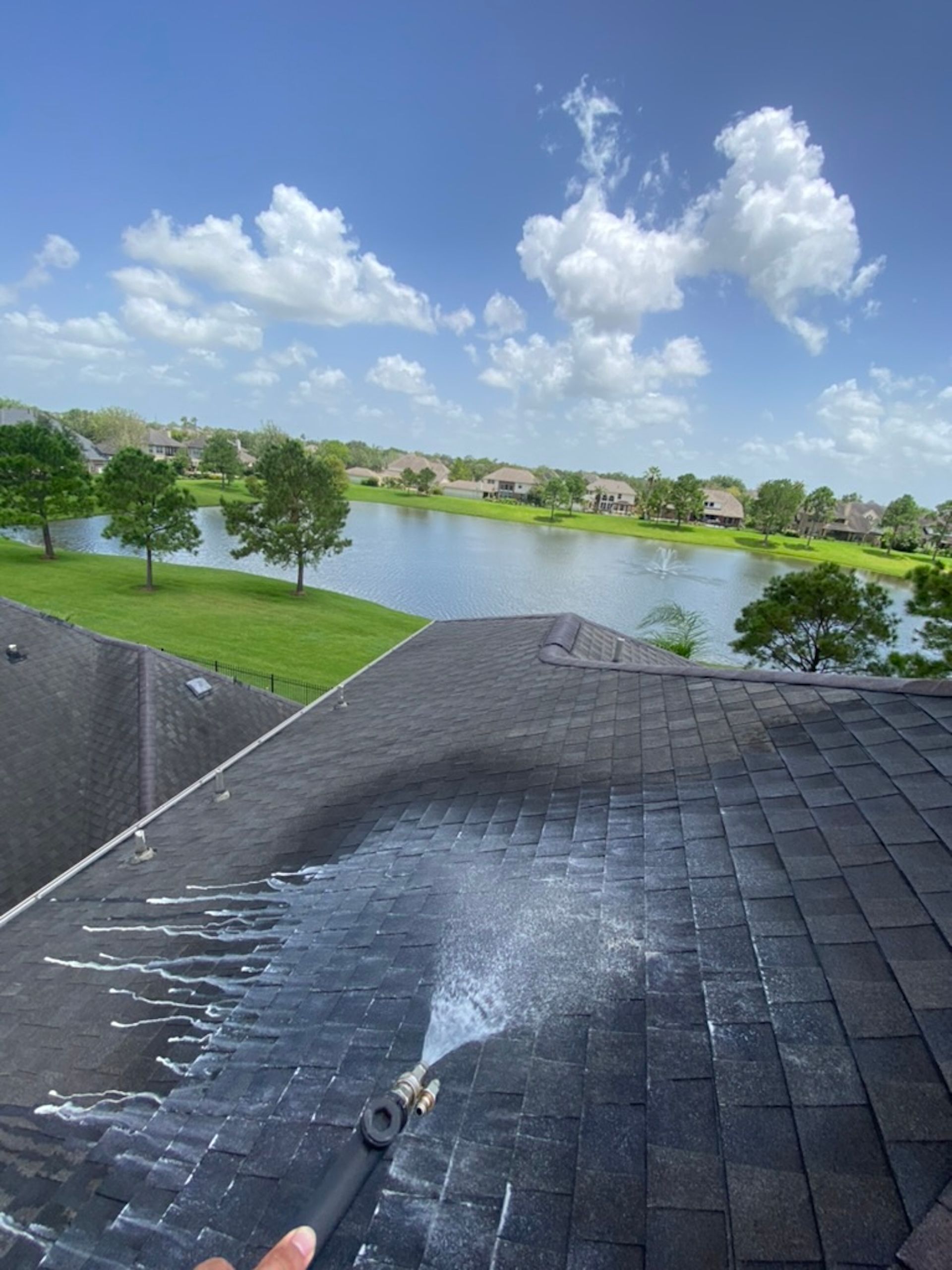 Water spraying across a dark roof shingles, overlooking a lake, green lawn, and cloudy blue sky.