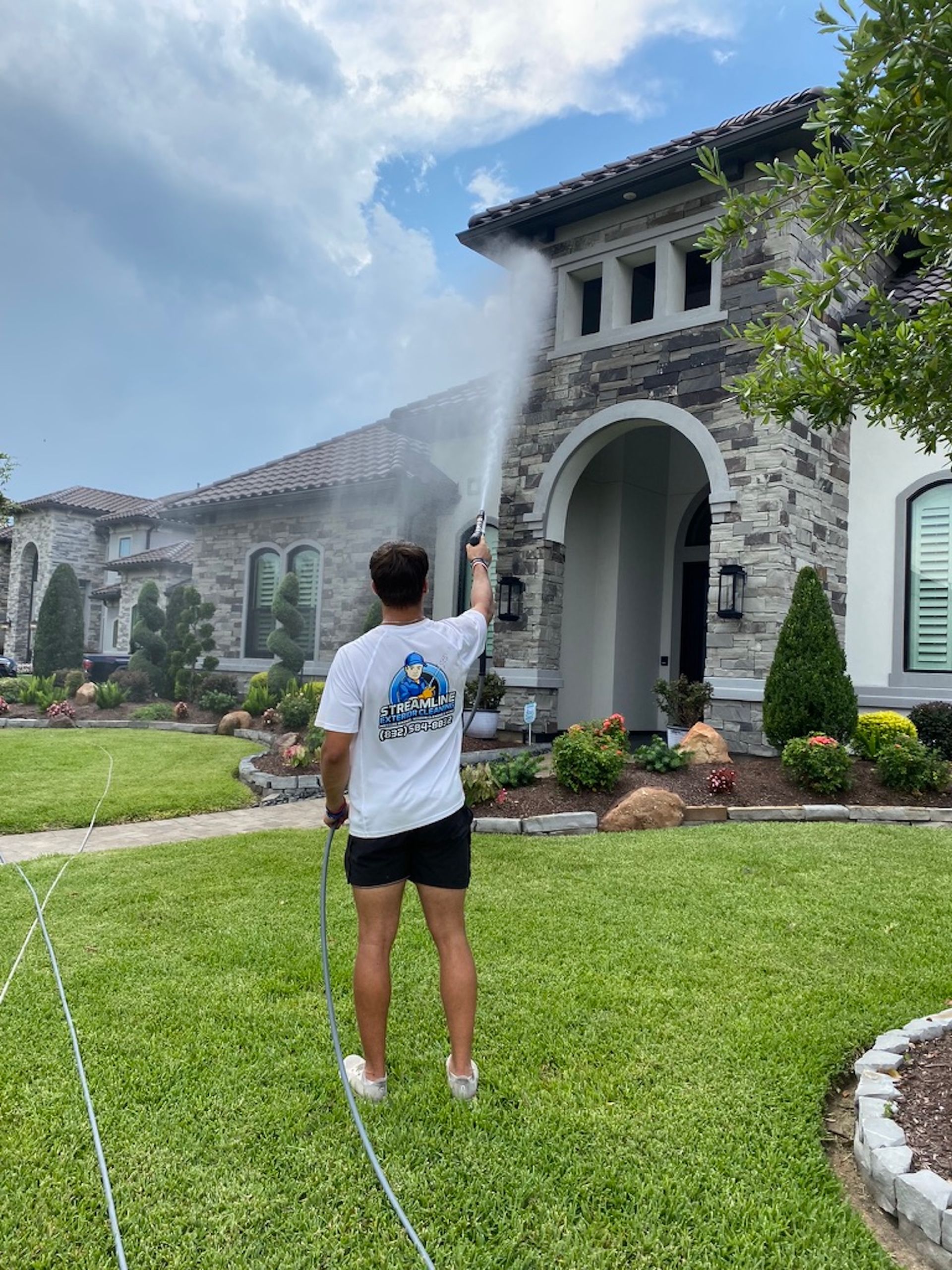 Person spraying water on a large stone mansion lawn on a sunny day