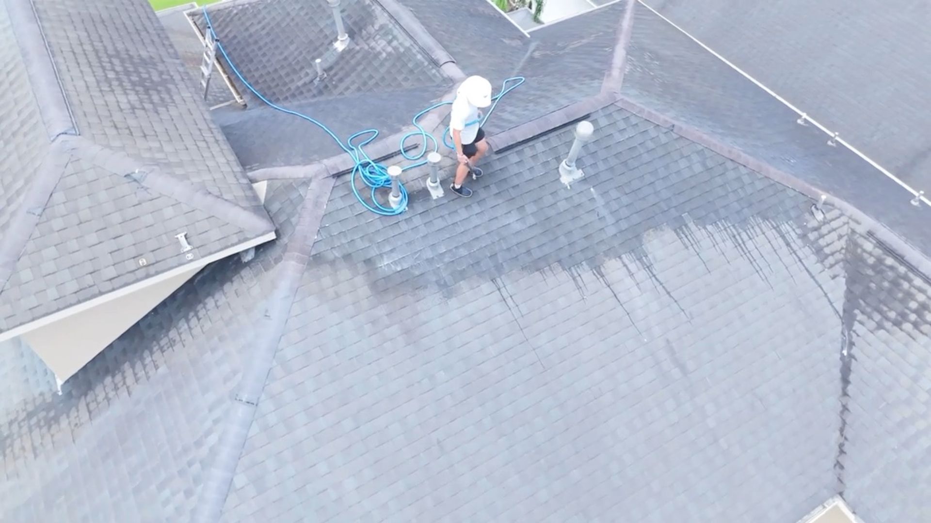 Worker on a gray shingled roof using tools near a skylight and safety gear