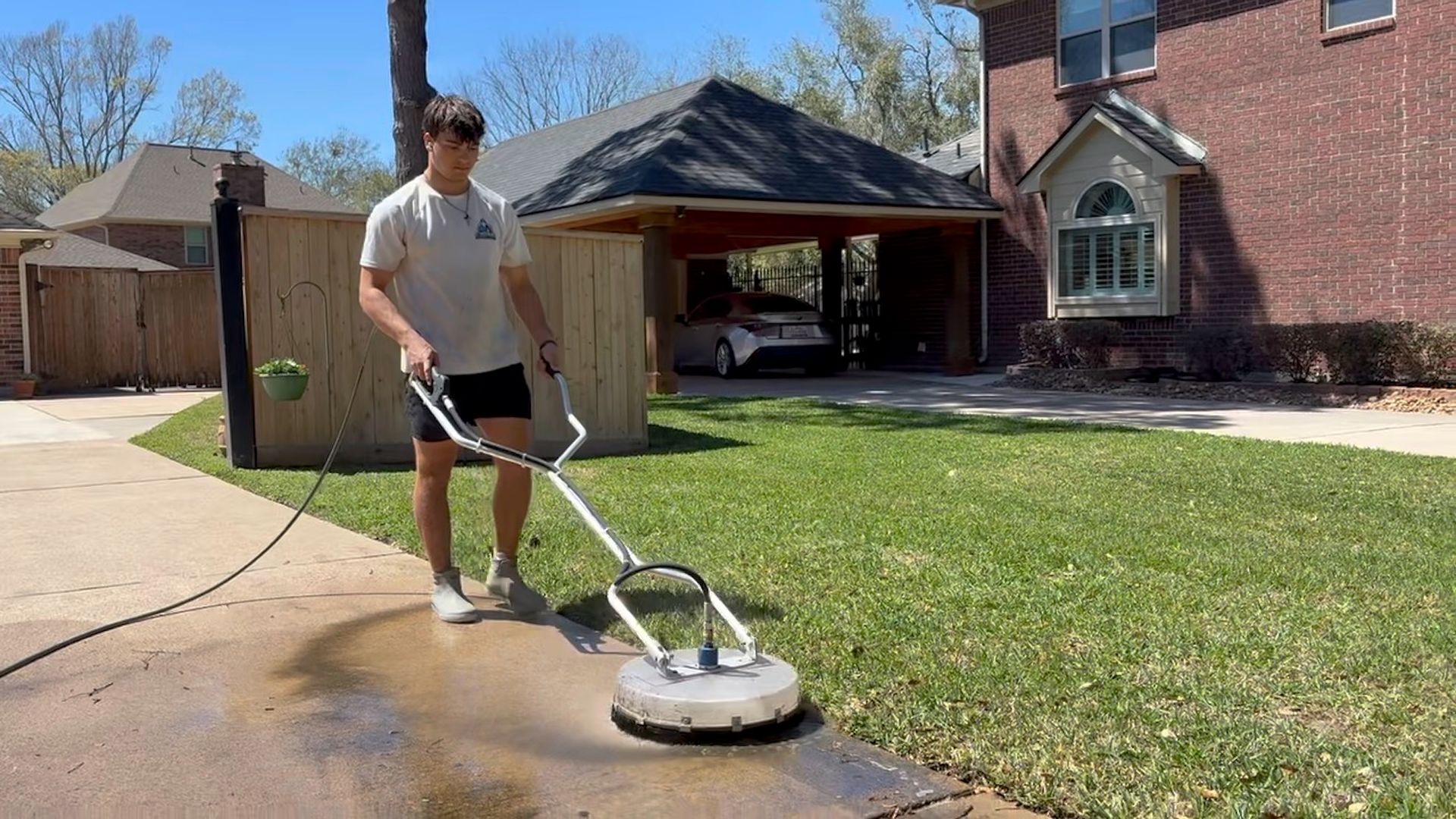 Person pressure washing a driveway beside a house on a sunny day