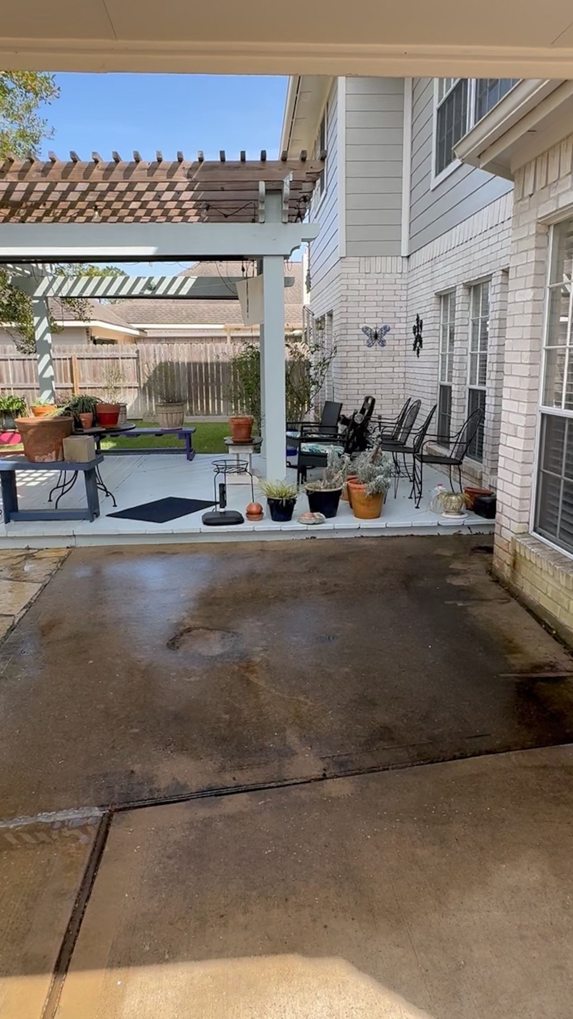 Covered patio with wet concrete, potted plants, chairs, and a white house exterior with sliding doors.