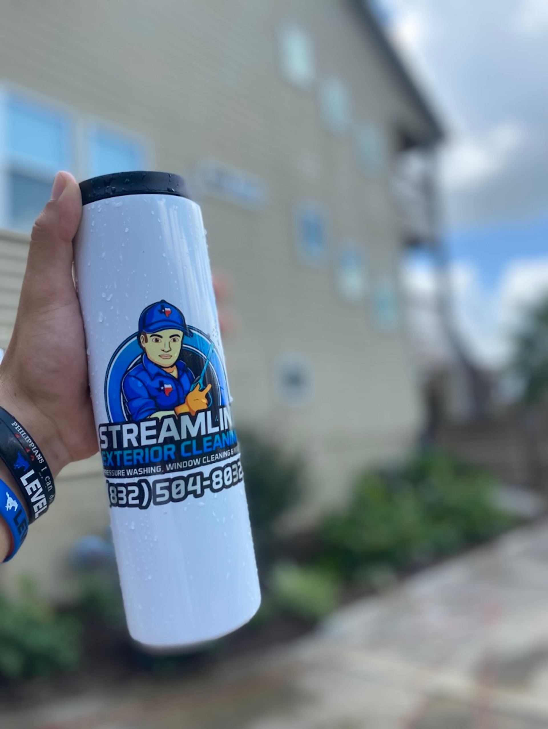 Hand holding a white Streamline water bottle with a blue logo and phone number outdoors.