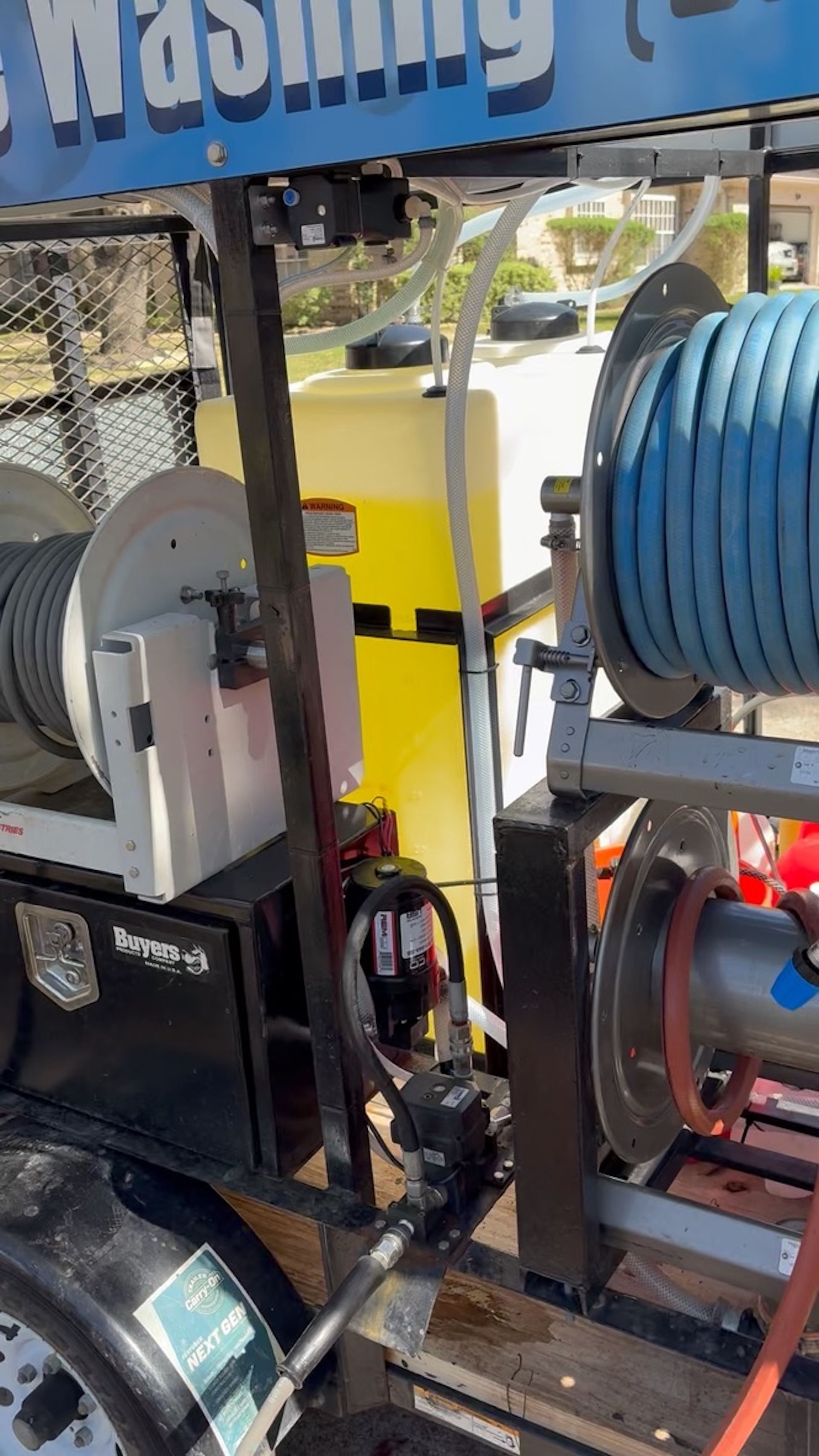 Car wash equipment with blue hose reels, pressure washer and cleaning tools in a metal rack.