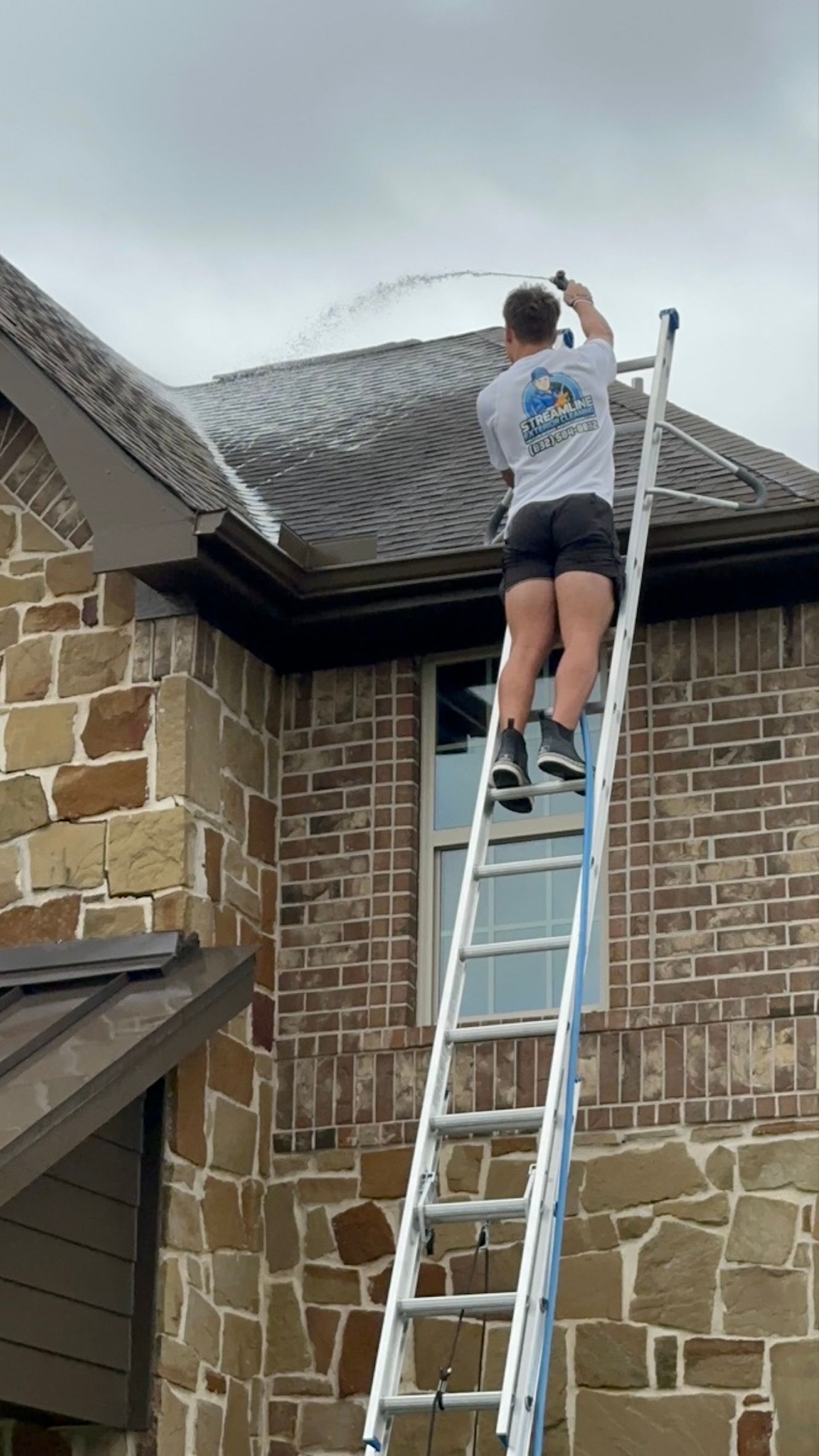 Person on a ladder cleaning the roof edge of a brick house