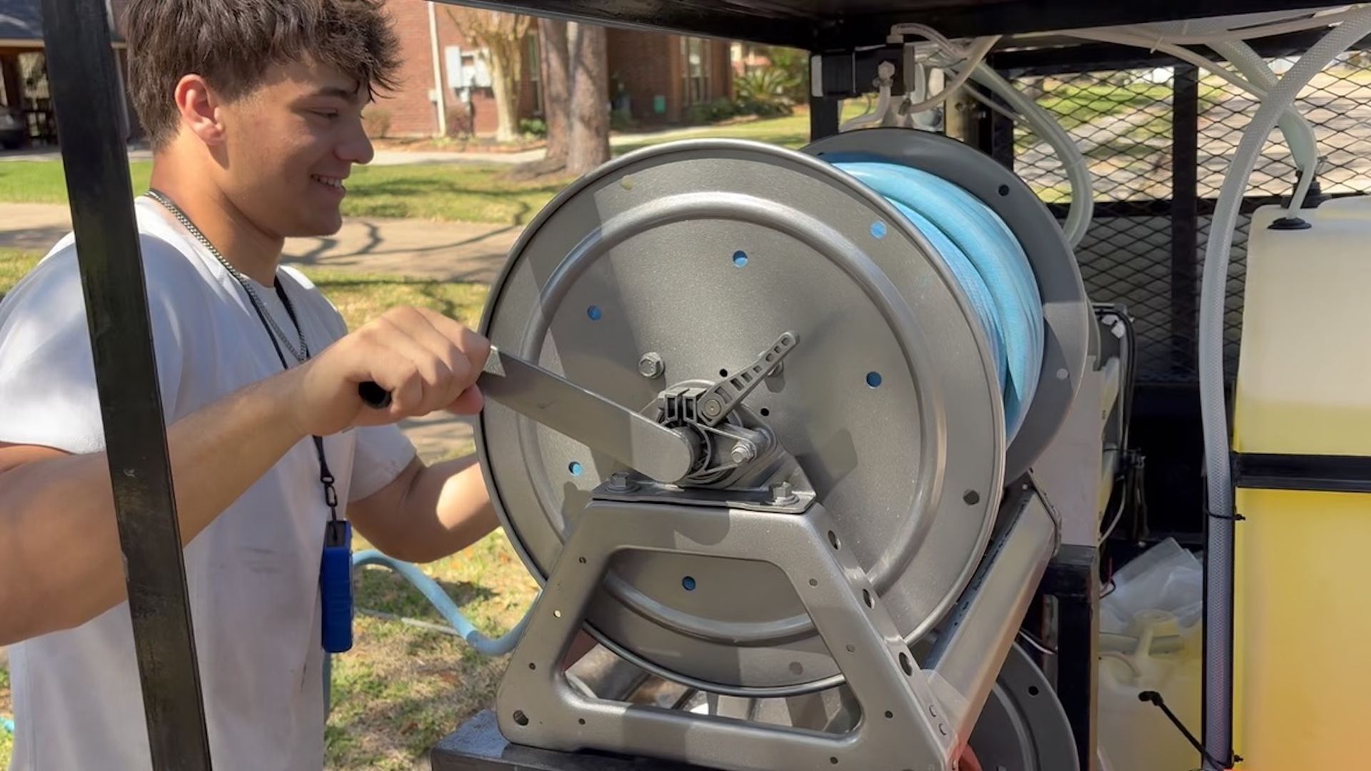 Person cranks a large blue hose reel on a trailer outdoors.