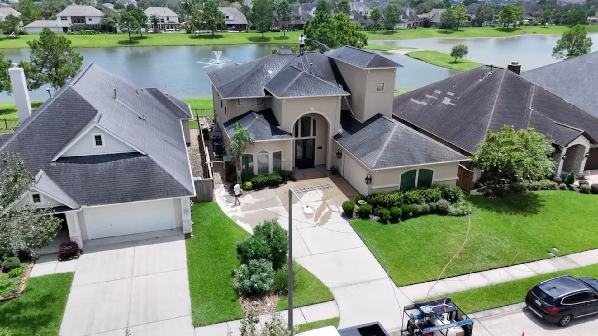 Aerial view of a large suburban house with driveway, lawn, and a lake behind it