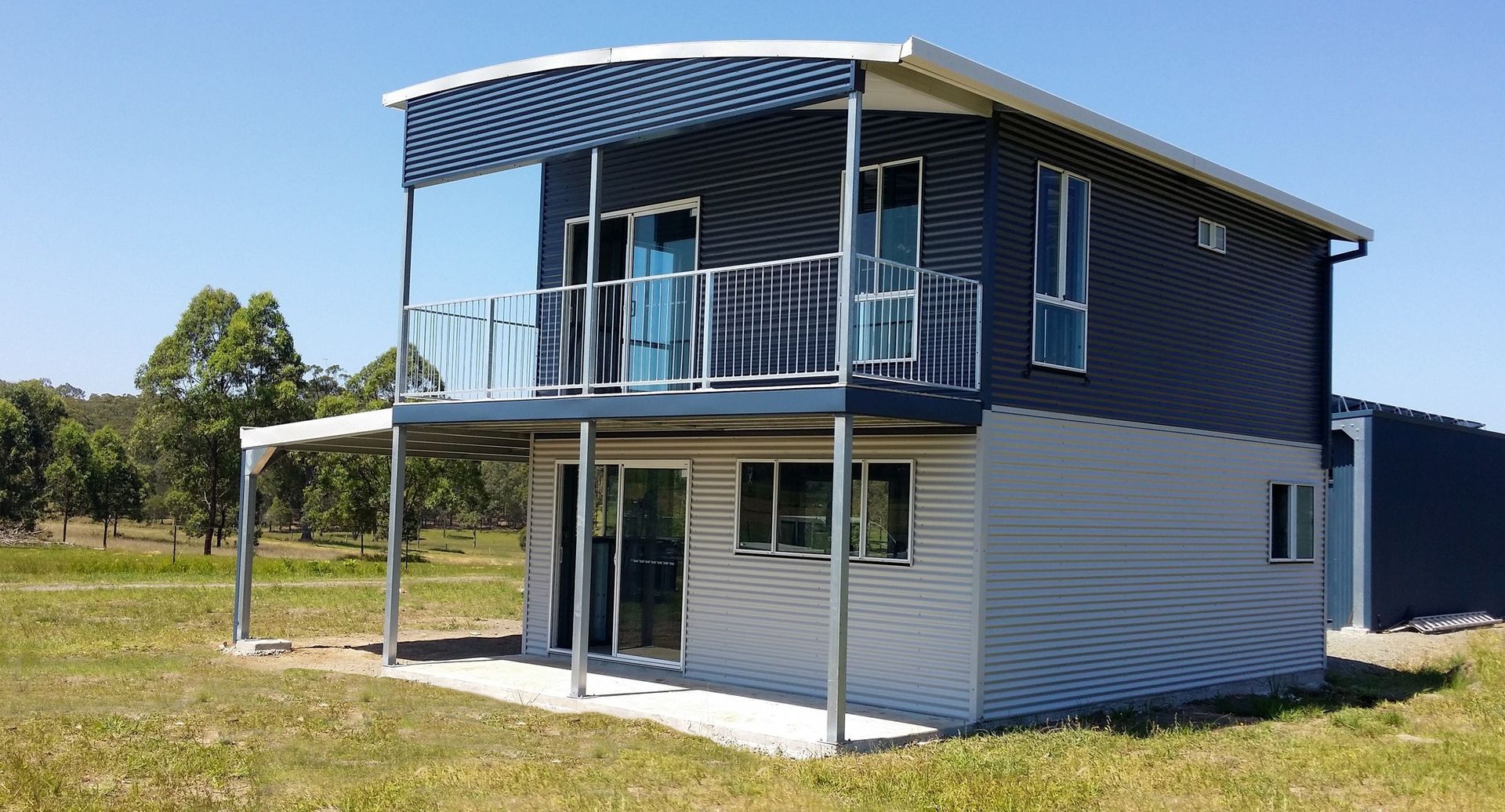 A small house with a balcony is sitting in the middle of a grassy field.