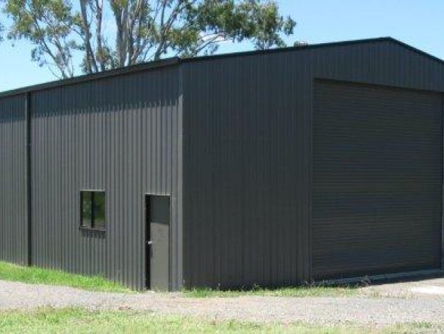 A large black metal building with a garage door and a window.