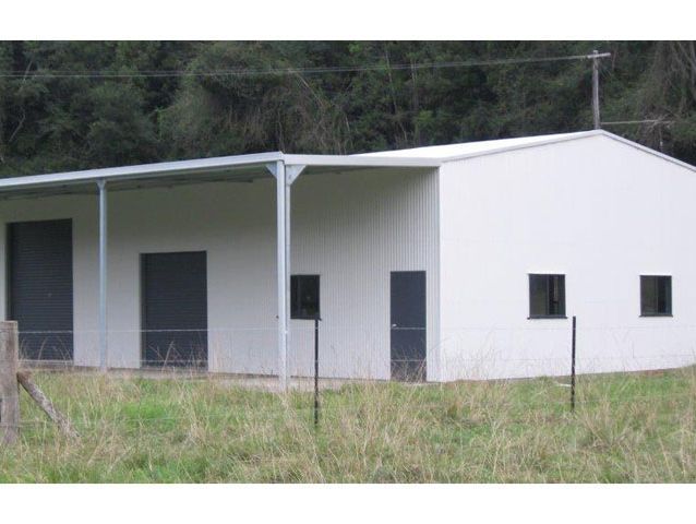 A white building with black doors and windows is in the middle of a grassy field.