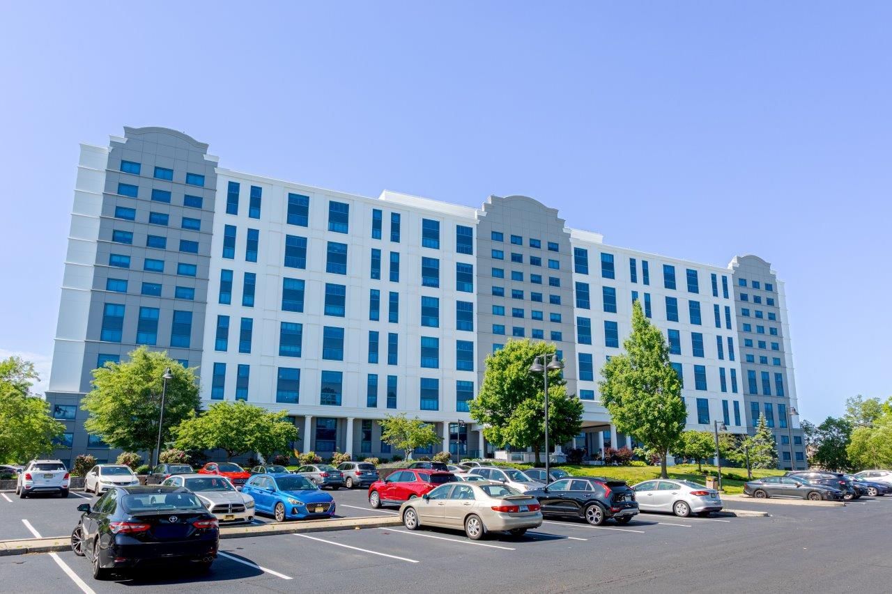 Large white and gray building with parking lot and cars on a sunny day