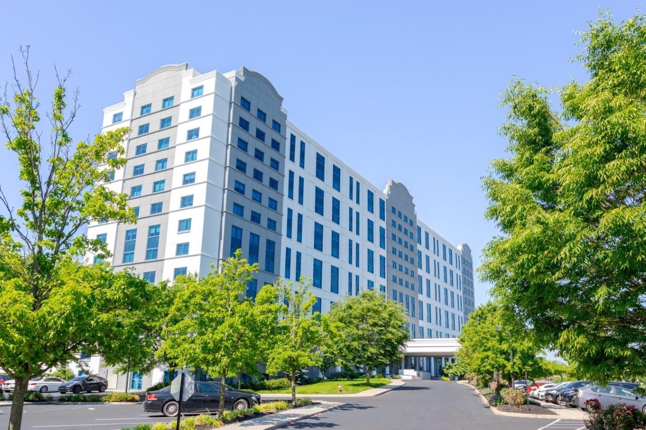 Large white and gray building with parking lot and cars on a sunny day