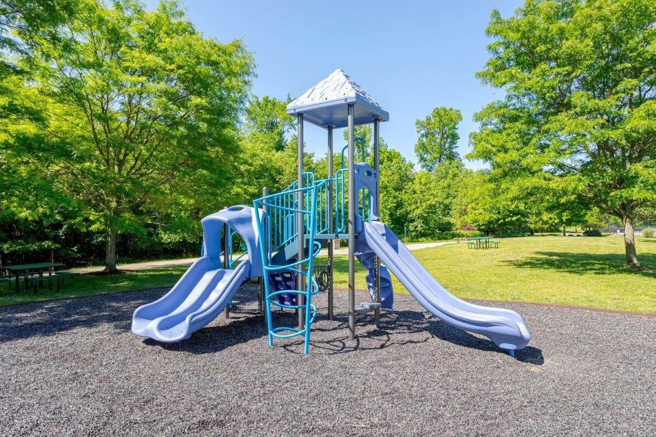 Blue playground slide structure on a woodchip playground surrounded by green trees and grass.