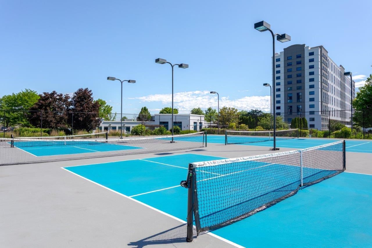 Outdoor pickleball courts with turquoise surface, net, and nearby apartment buildings under a blue sky