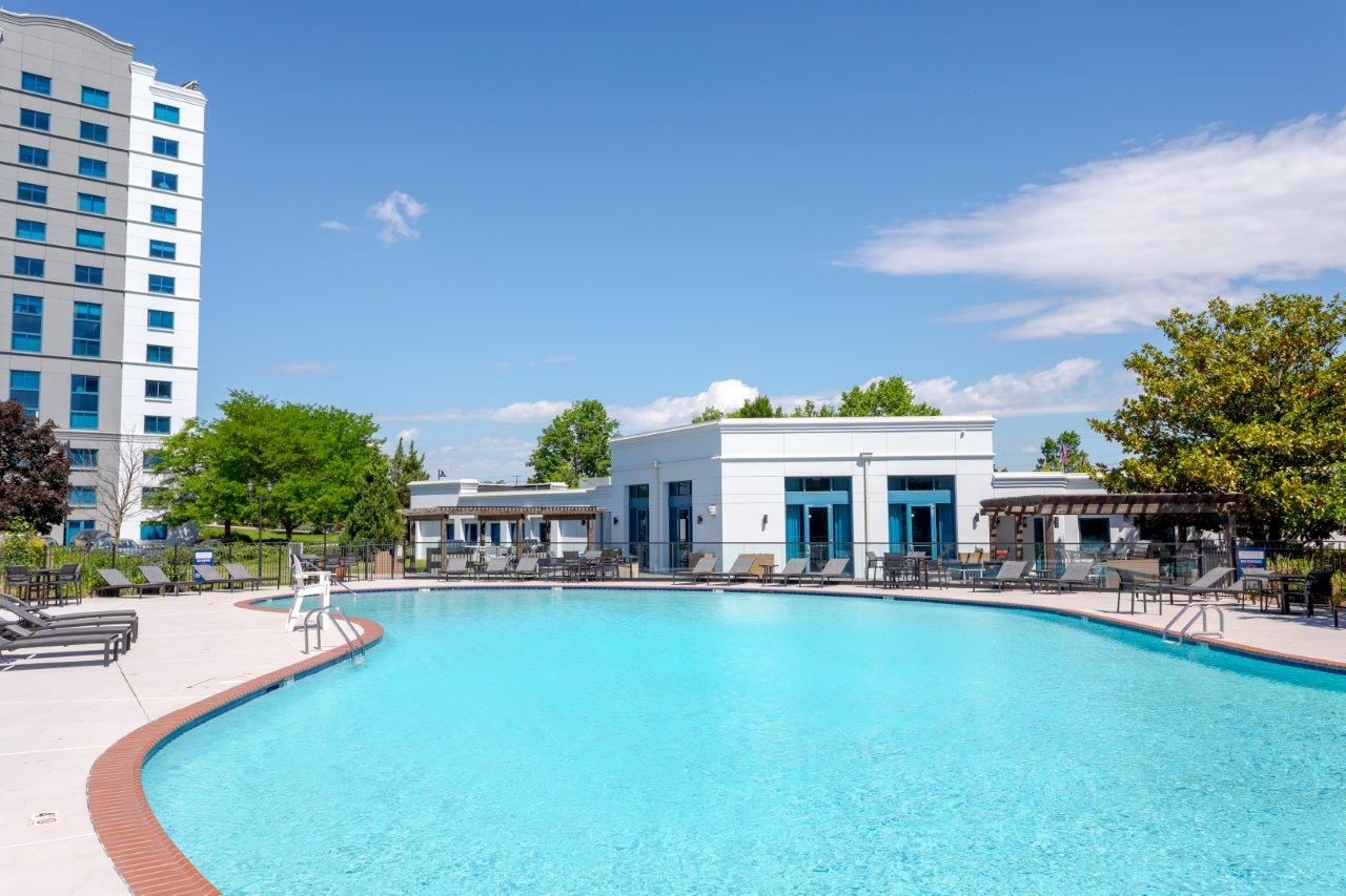 Outdoor pool with turquoise water, lounge chairs, and a white resort building under a blue sky