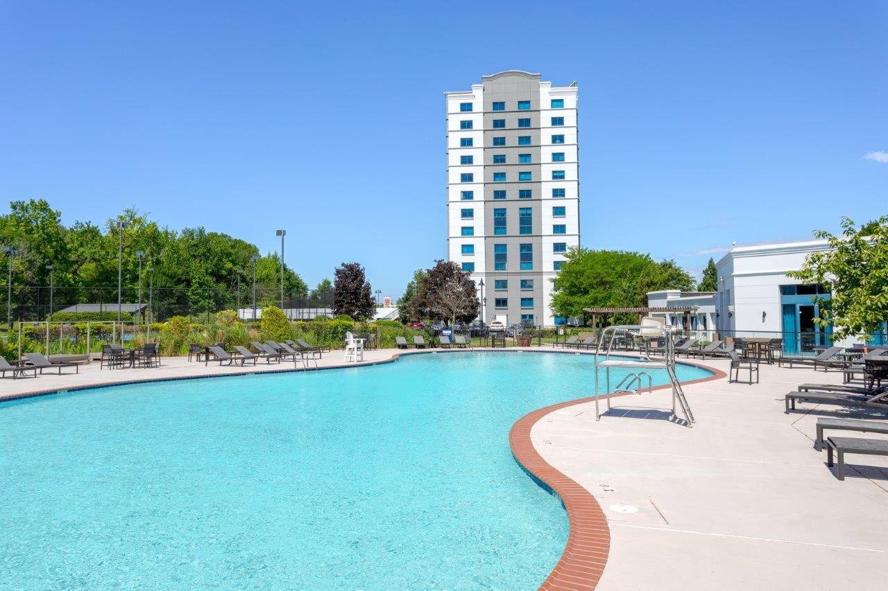 Outdoor pool with turquoise water, lounge chairs, and a tall white building under a clear blue sky