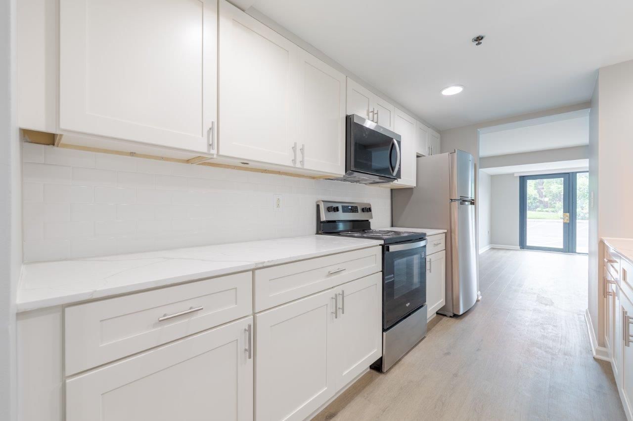 Bright white galley kitchen with stainless appliances and a view to a hallway and windowed door