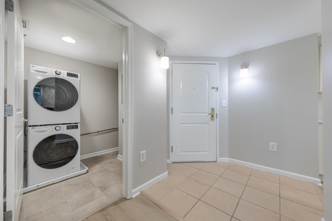 Laundry room with stacked washer and dryer, beige tile floor, gray walls, and white door