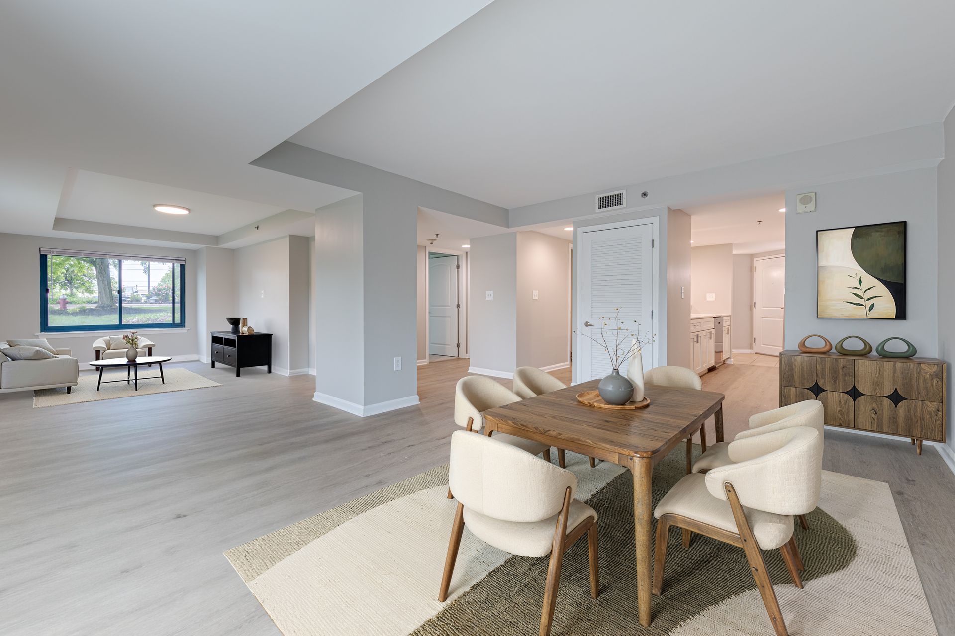 Bright open-concept living and dining room with light wood floors, white walls, and modern furniture.