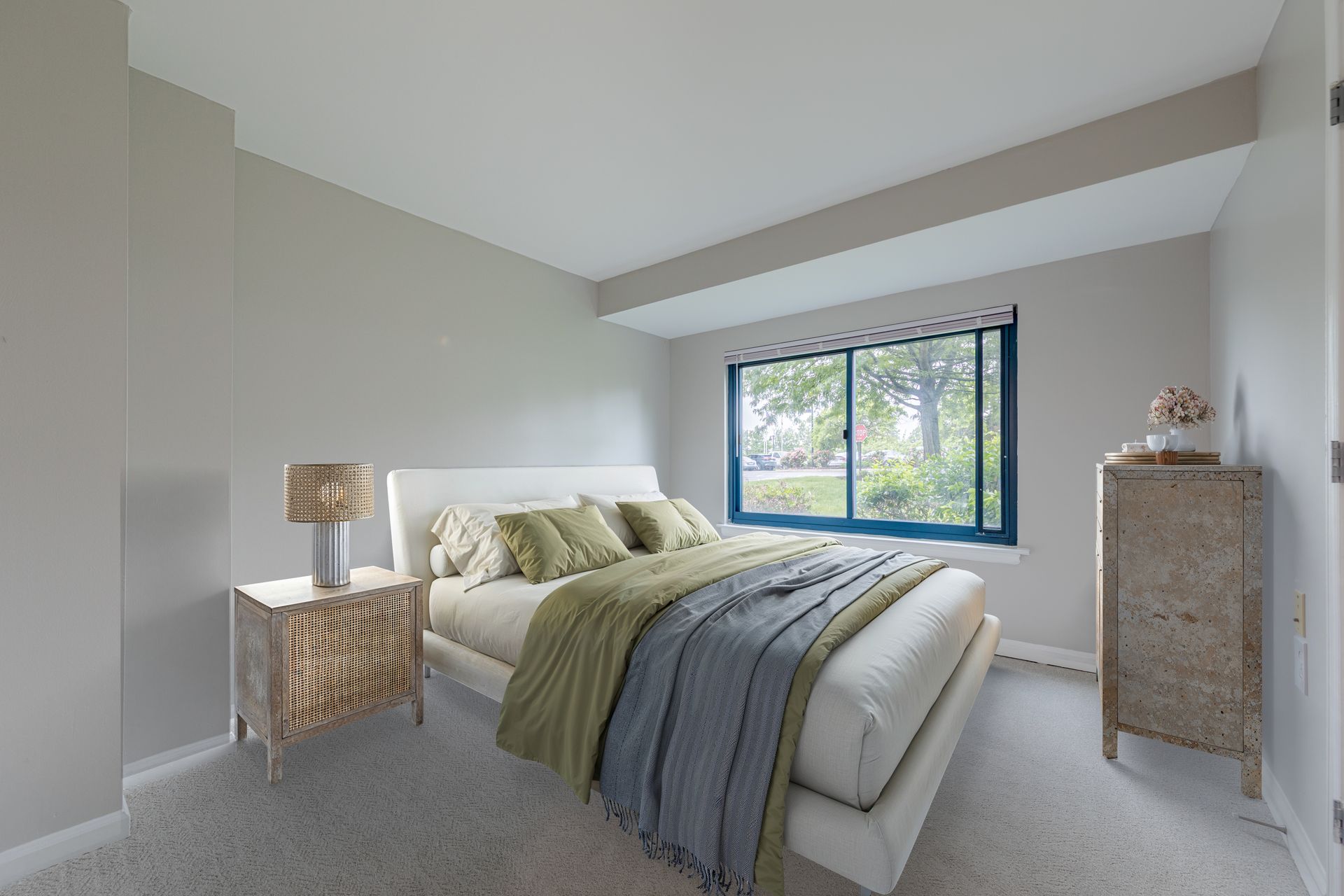 Bright bedroom with a bed, two nightstands, and a large window with a view outside.