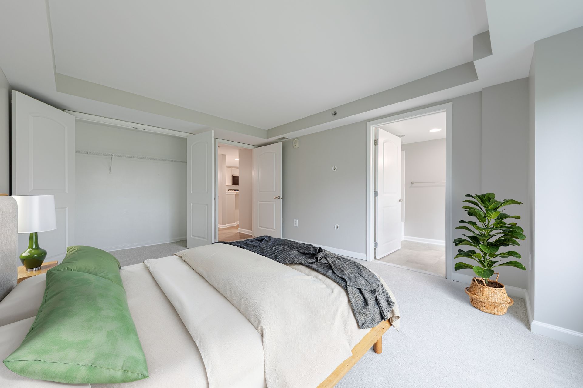 Bright modern bedroom with a white bed, green pillow, gray throw, and open closet and bathroom doors