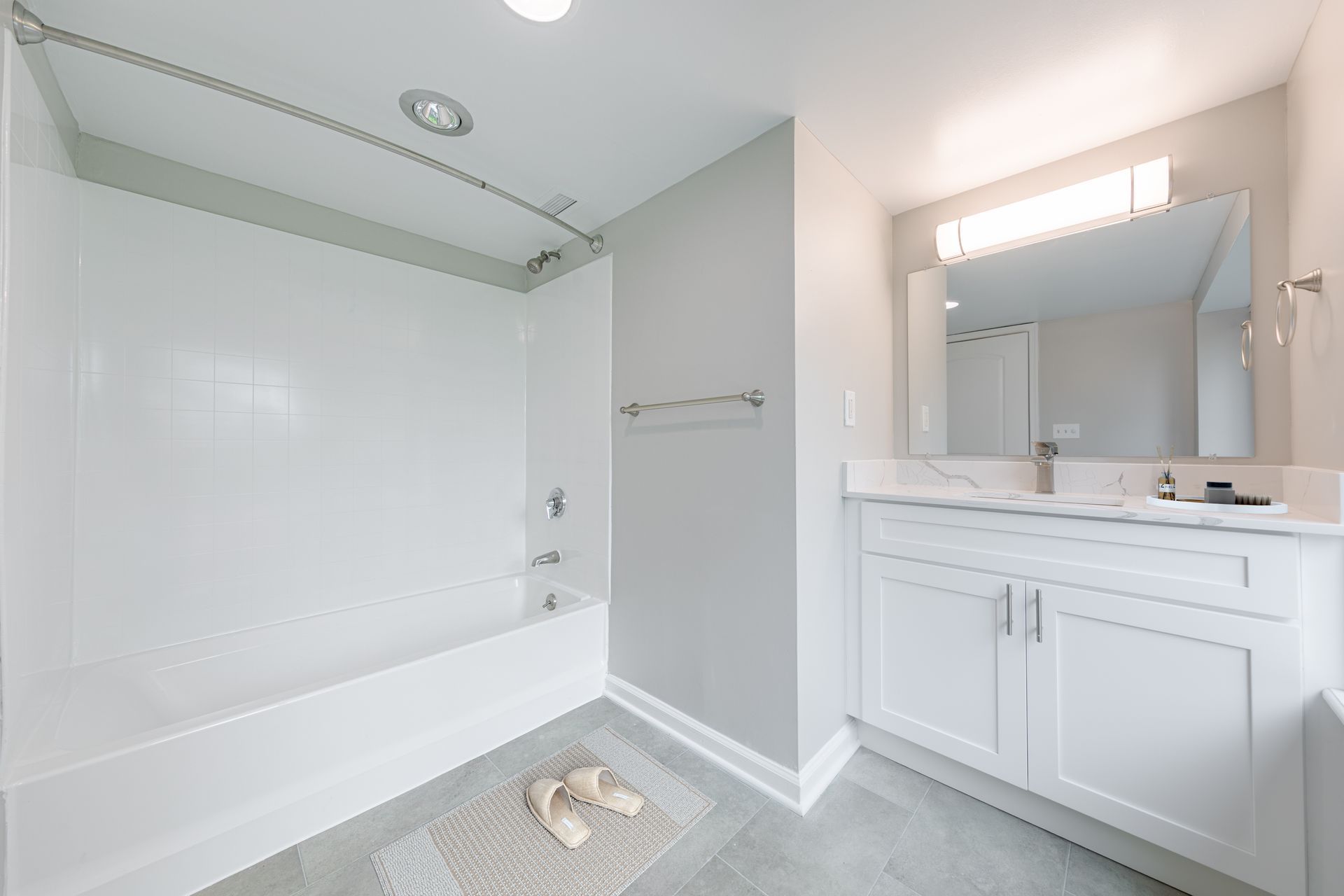 Bright modern bathroom with white vanity, large mirror, and tiled tub/shower area