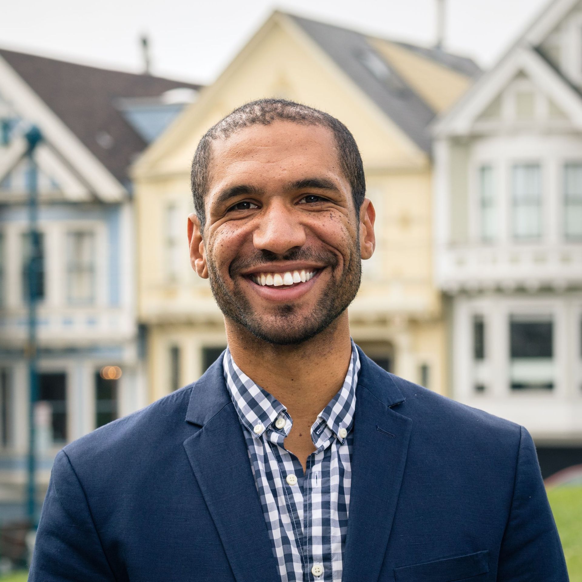 Man in navy blazer smiles in front of colorful houses.