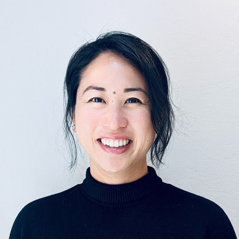 Woman with dark hair smiles, wearing a black turtleneck, against a white background.
