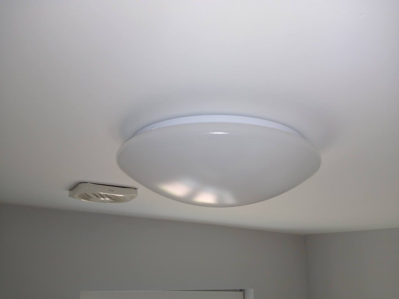 A round LED IP rated bathroom light fitting installed on the ceiling next to an extractor fan.