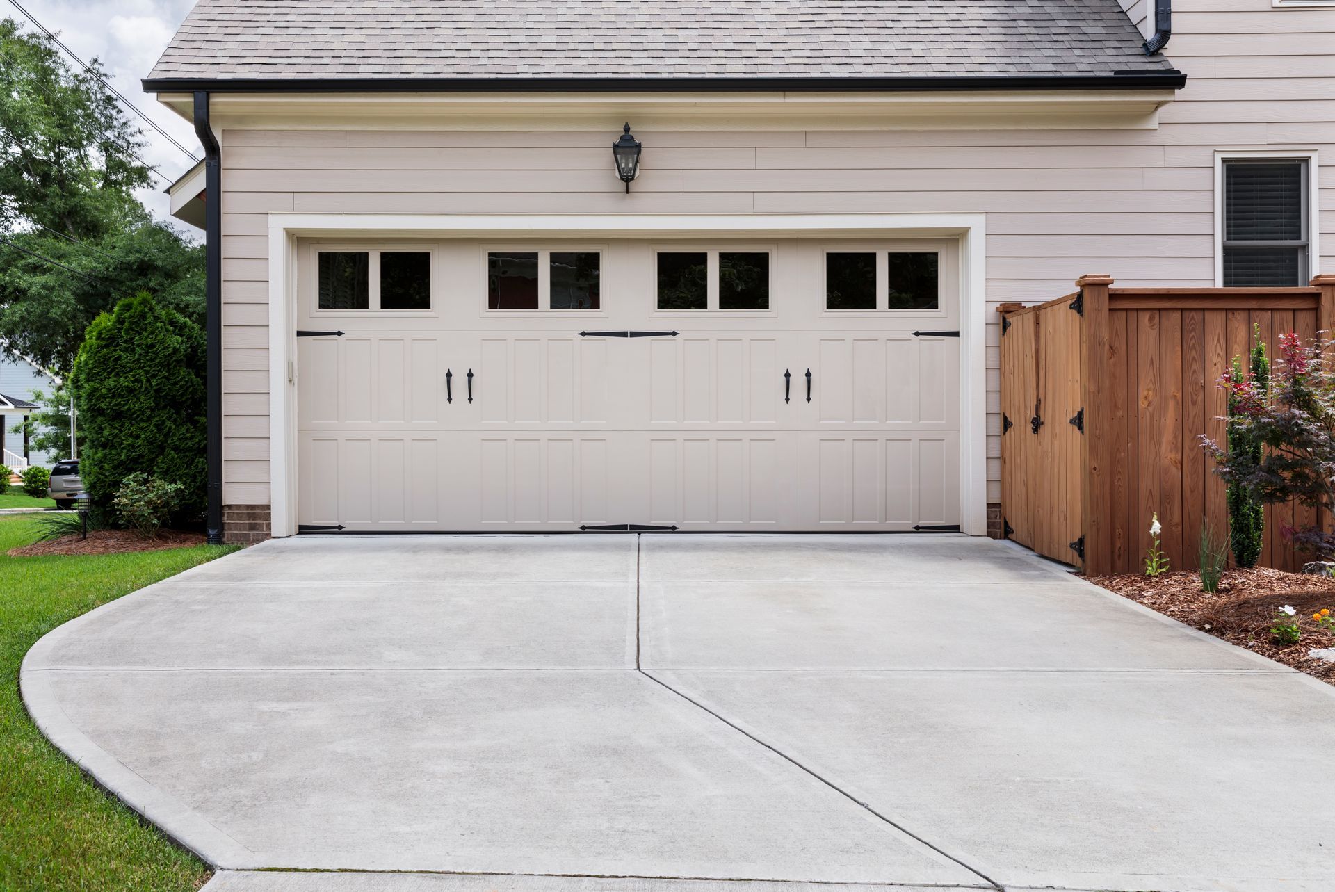 Two-car garage with white doors and a concrete driveway in front of a beige house