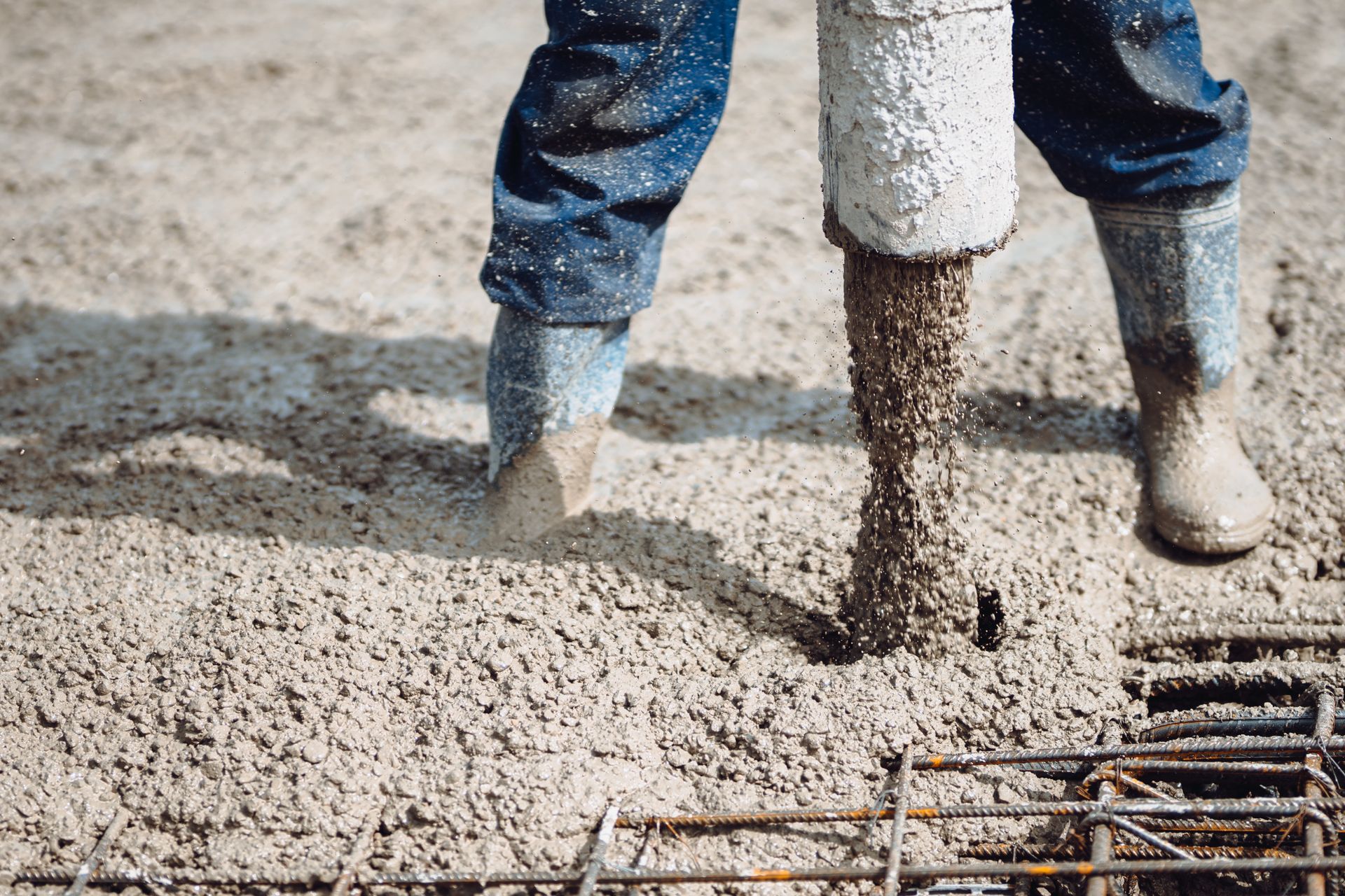 Concrete being poured around rebar by a worker in boots on a construction site