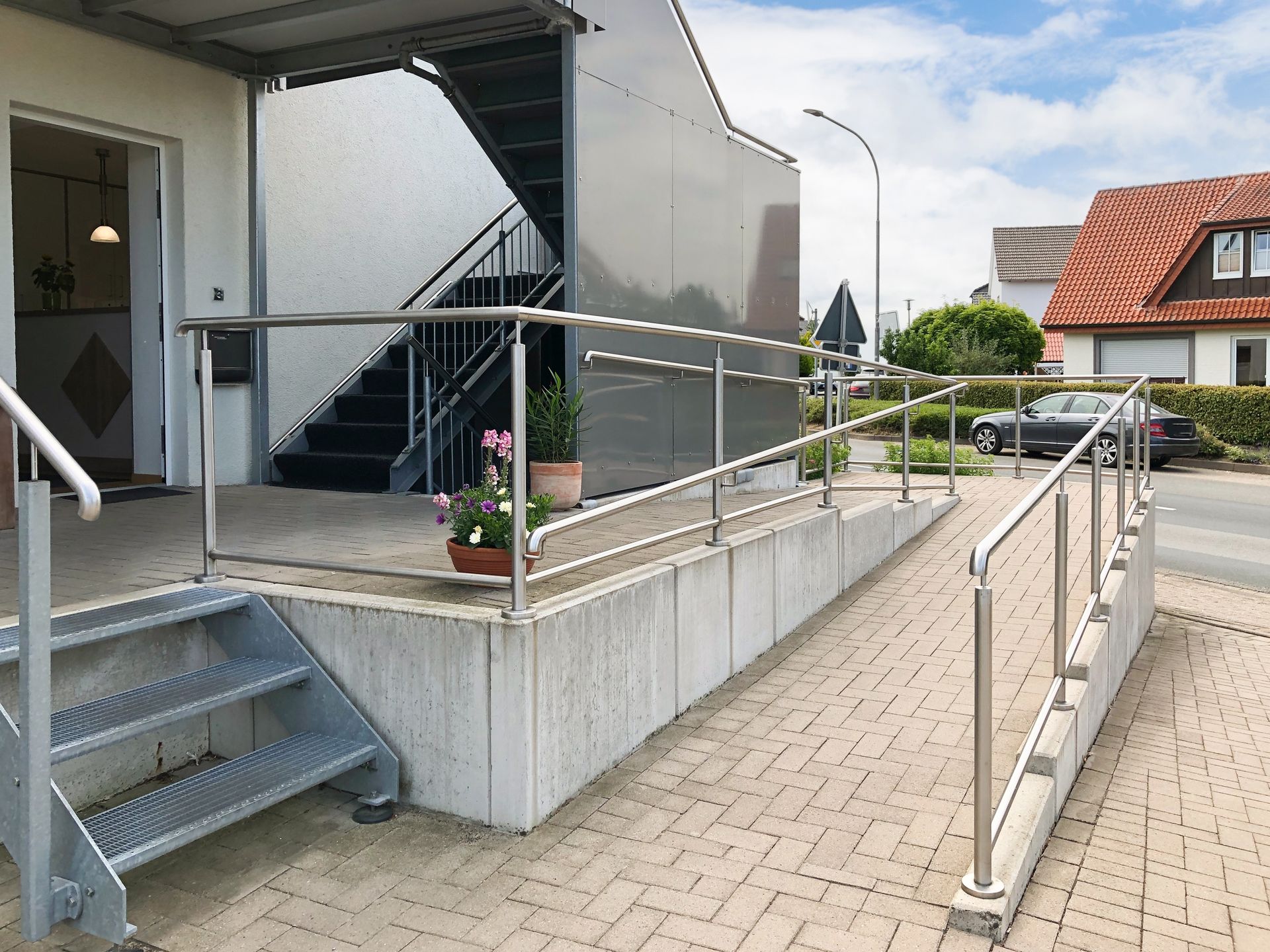 Accessible building entrance with ramp, metal handrails, stairs, and potted flowers